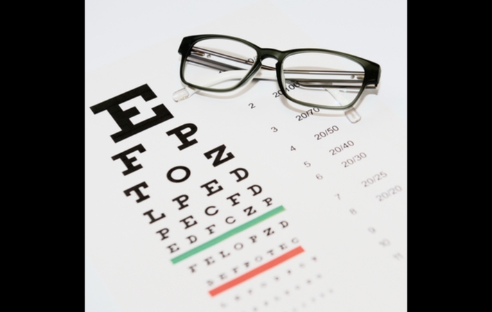Image of a Snell eye chart laid out on a table with a black pair of glasses sitting on top of it.