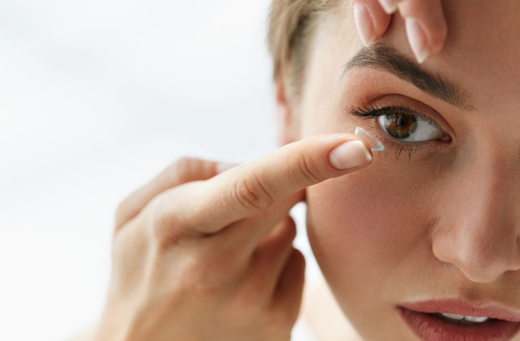 A woman putting a contact lens into her right eye.