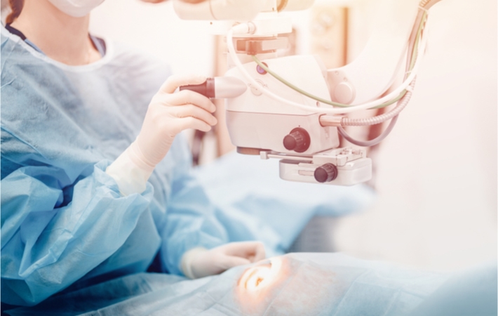 An eye surgeon positions a laser above a patient's eye while laying on the medical bed.