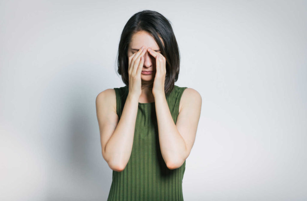 Woman standing against a grey background rubbing her eyes.