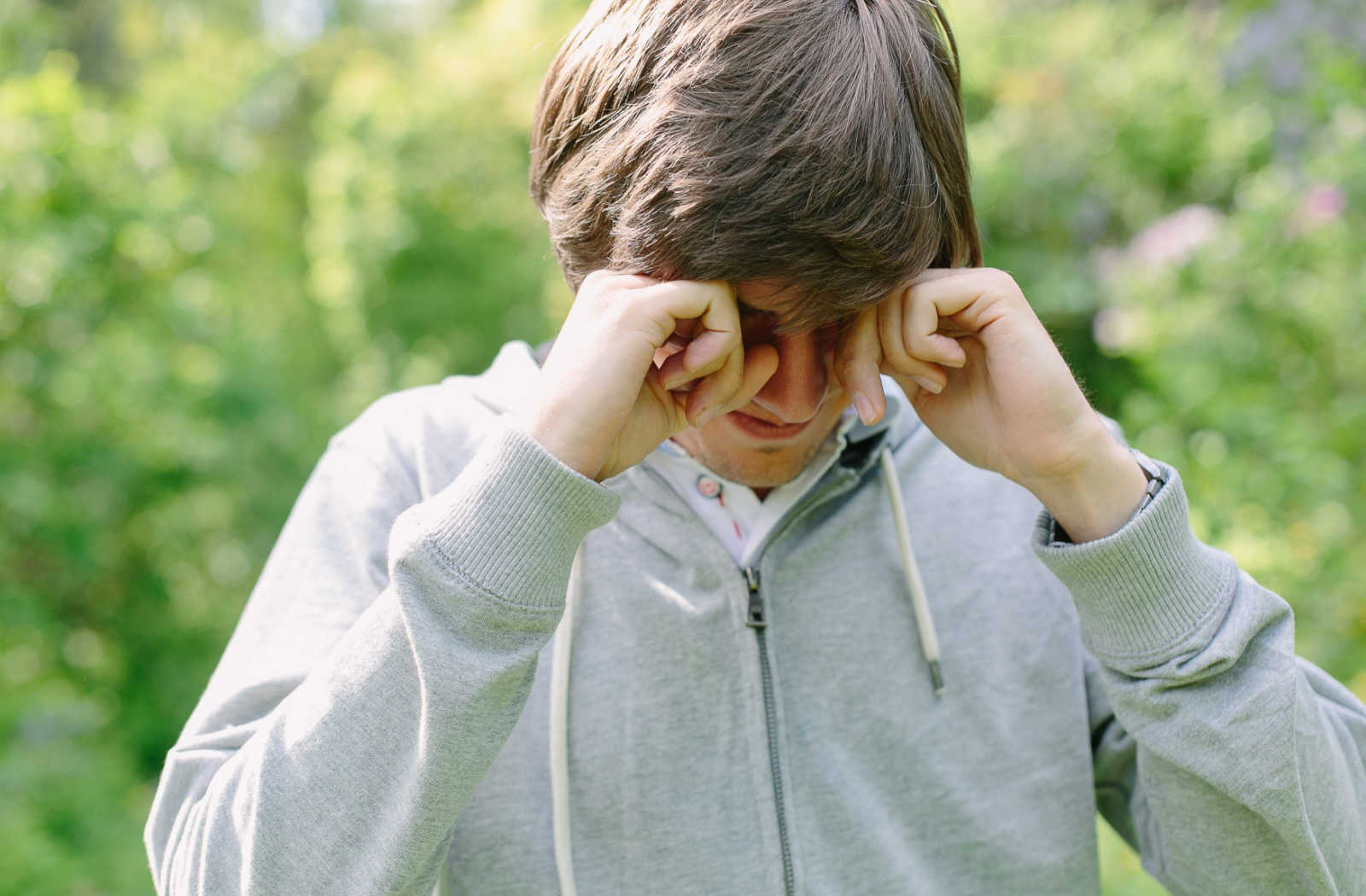 A young man outside rubbing his eyes.