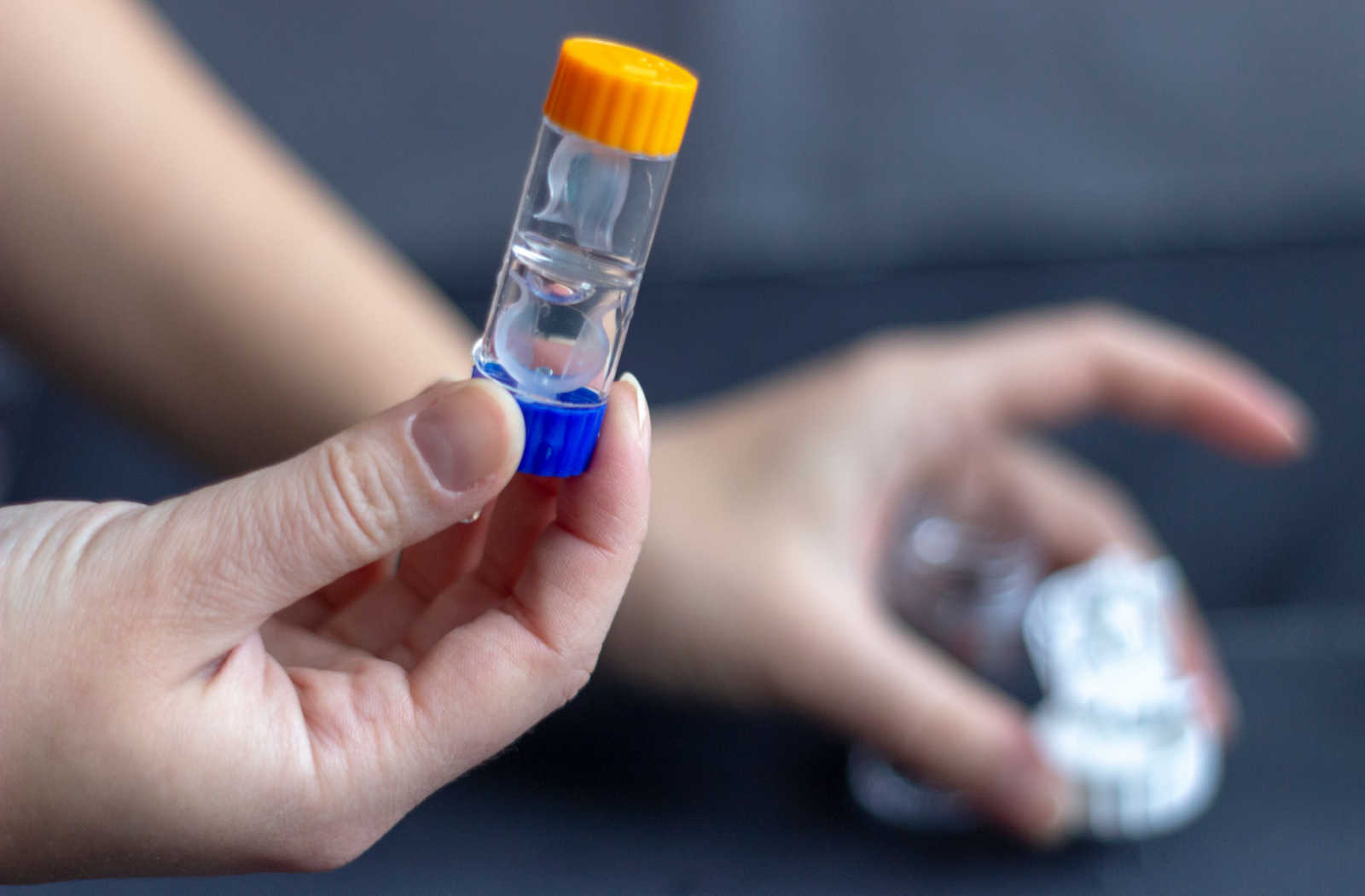 A close-up of a hand holding Orthokeratology lenses in the container.
