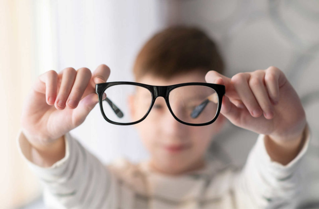 A young boy holding up a pair of glasses to the camera.