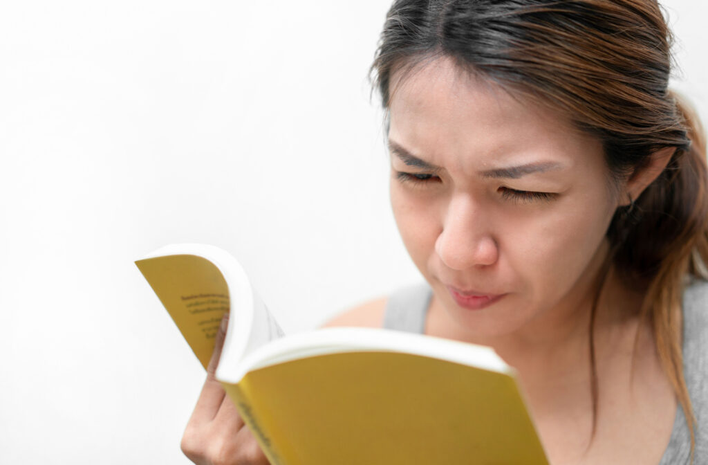 Close-up of a young woman holding a yellow book and squinting to read it.