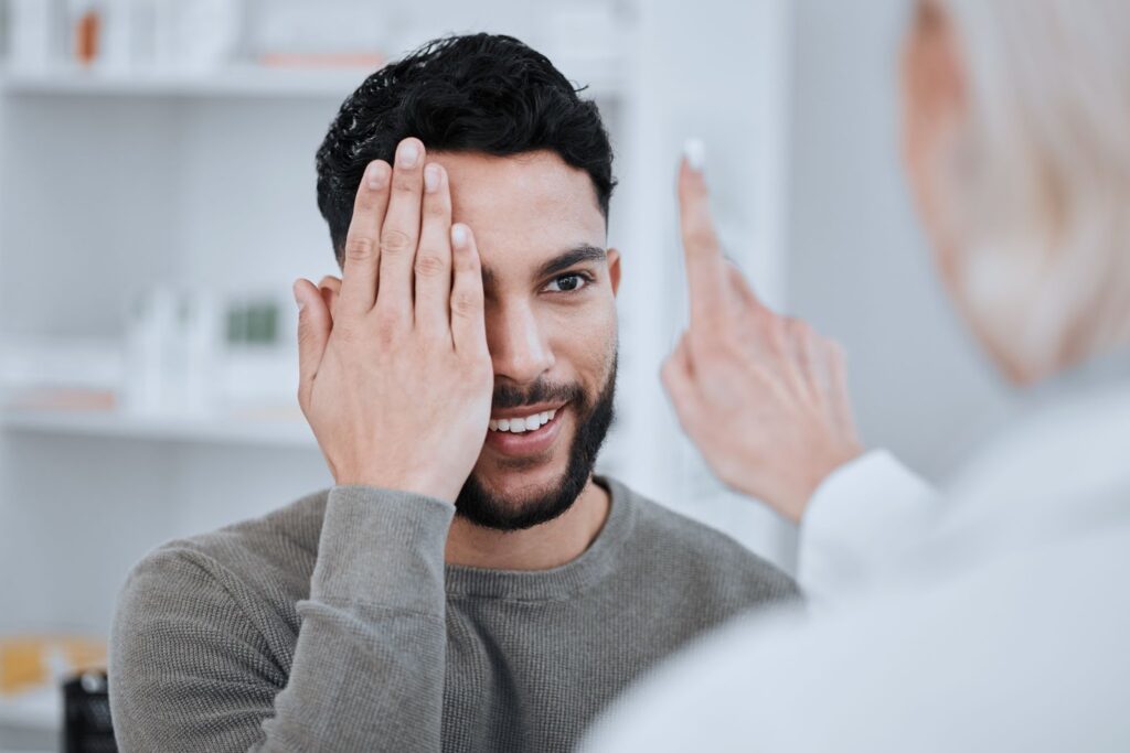 A man covering his right eye with his right hand during an eye exam to test eye misalignment.