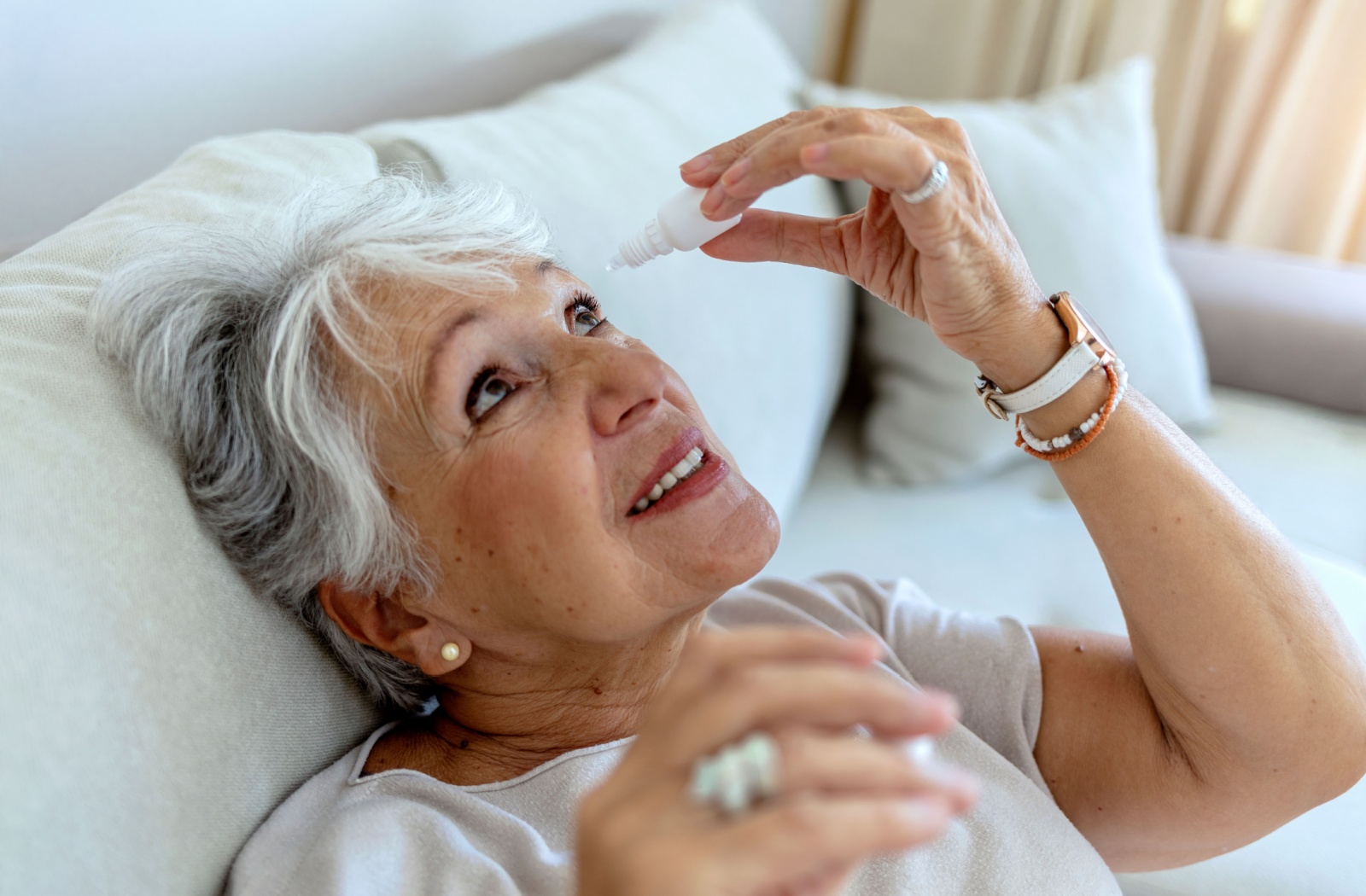 An older woman is placing eyedrops in her eyes before going to bed.