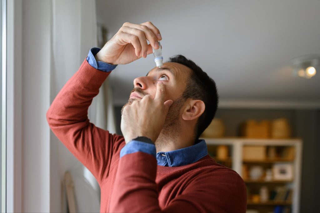 A man is placing eye drops in his eye.