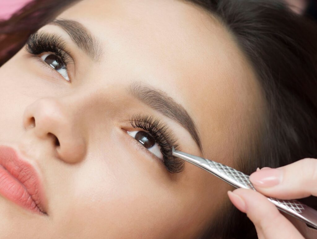 Woman getting fake eyelashes applied, highlighting her eyes and the eyelash tweezers.