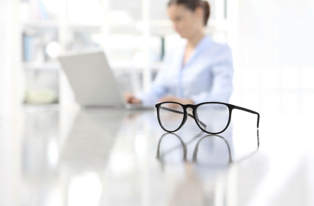 A pair of glasses sit in front of a typing on a laptop computer.