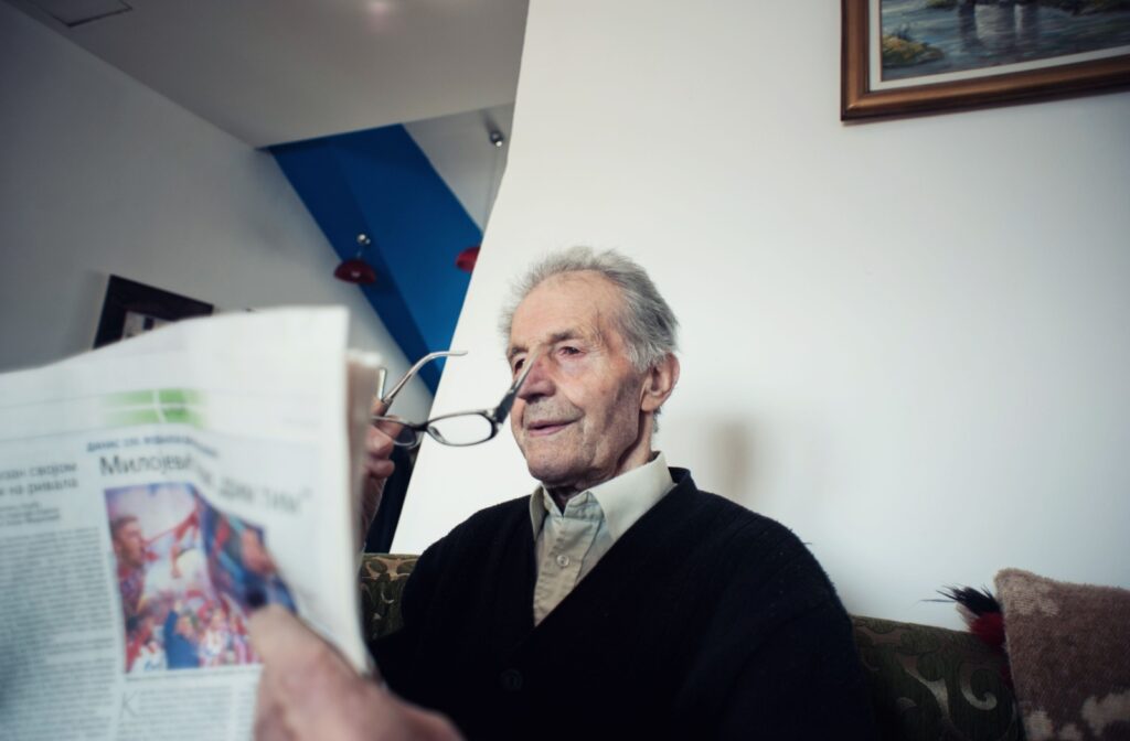 A senior reading the newspaper removes their glasses, struggling to see clearly.