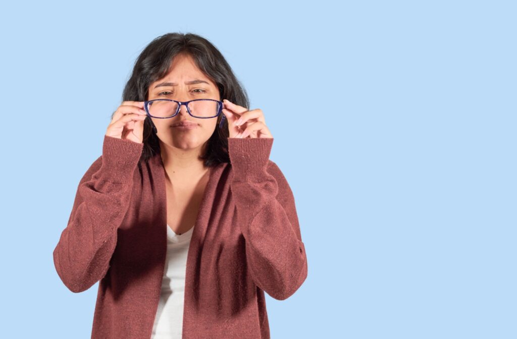 A young adult pulls glasses out from their face as they realize their prescription is off.