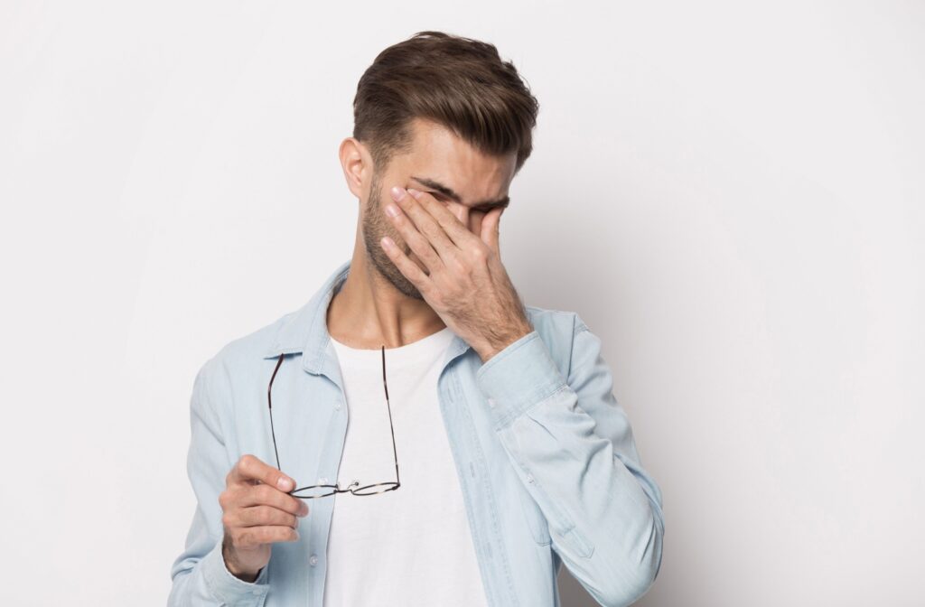 A young mam in front of a white background taking off his glasses and rubbing eyes.