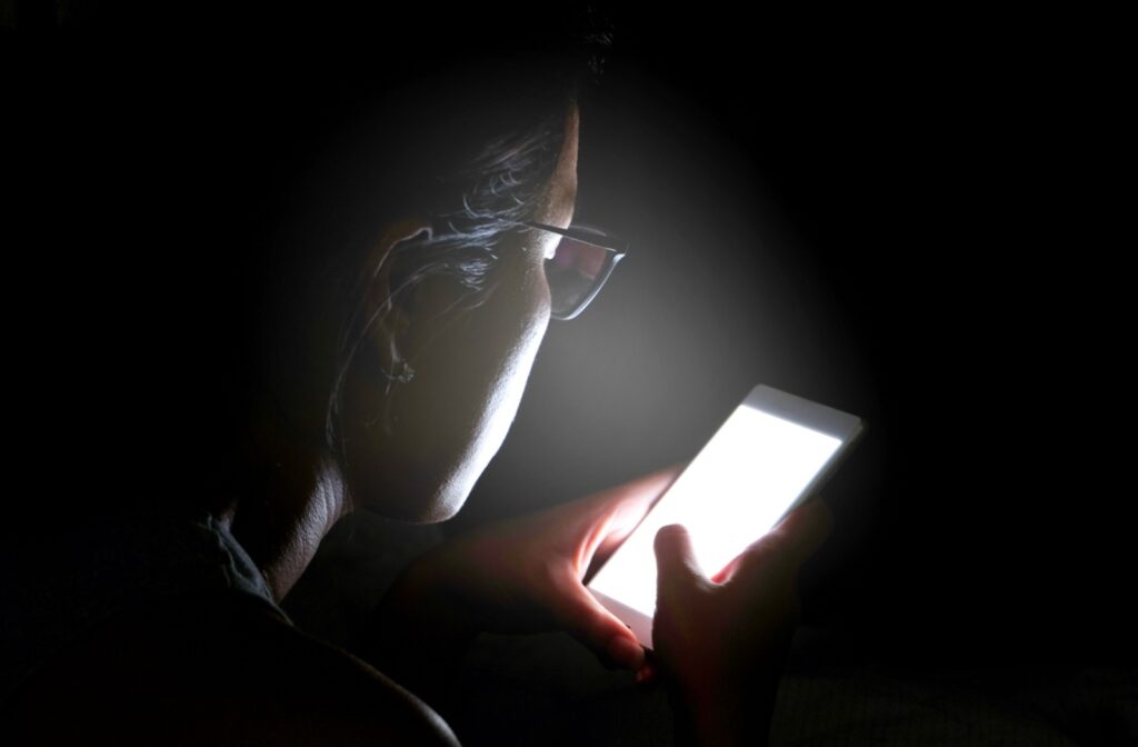 Woman with glasses using mobile phone in the dark.
