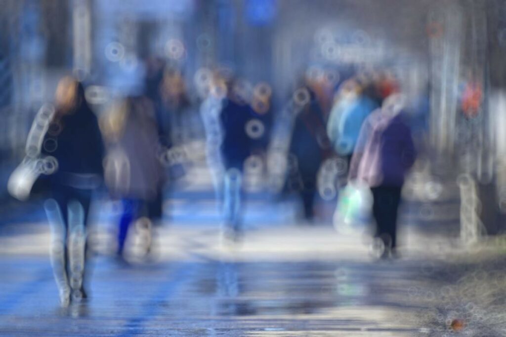 A photograph of a busy street scene rendered with severe blur and donut-shaped bokeh artifacts to simulate the visual experience of someone with cataracts or significant refractive errors, helping patients understand common vision-impairing conditions.